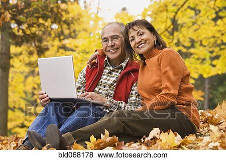 Hispanic couple using laptop sitting in autumn leaves View Large Photo Image Stock Photo - Hispanic couple using laptop sitting in autumn leaves. Fotosearch