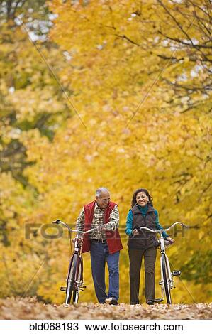 Stock Image - Hispanic couple walking bicycles in autumn. Fotosearch