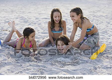 Stock Photograph - Hispanic girls burying Hispanic boy in sand. Fotosearch