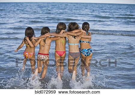 Stock Photo - Hispanic girls running through ocean surf. Fotosearch