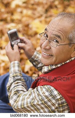 Stock Image - Hispanic man using cell phone outdoors in autumn. Fotosearch