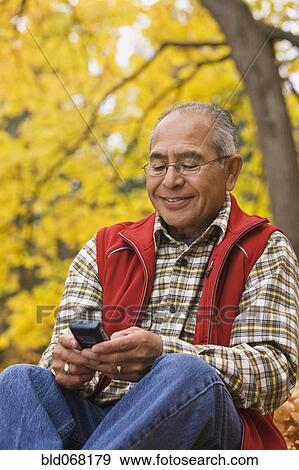 Hispanic man using cell phone outdoors in autumn View Large Photo Image Stock Photo - Hispanic man using cell phone outdoors in autumn. Fotosearch