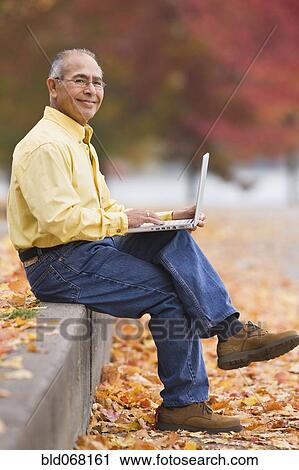 Stock Image - Hispanic man using laptop outdoors in autumn. Fotosearch