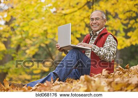 Hispanic man using laptop sitting in autumn leaves View Large Photo Image Stock Photograph - Hispanic man using laptop sitting in autumn leaves. Fotosearch