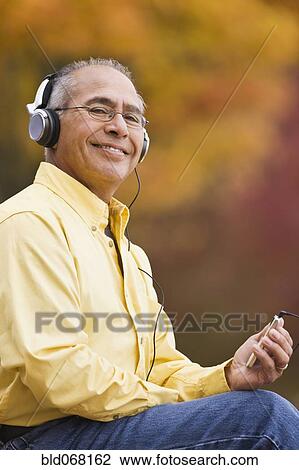 Stock Image - Hispanic man wearing headphones holding mp3 player. Fotosearch
