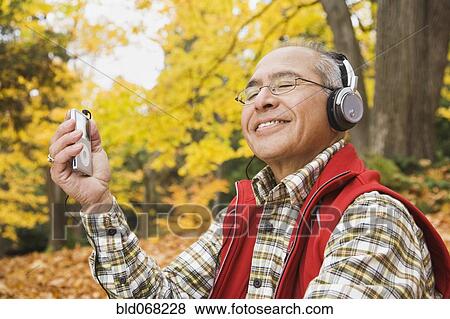 Stock Photo - Hispanic man wearing headphones holding mp3 player. Fotosearch