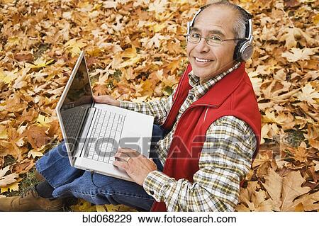 Stock Photo - Hispanic man wearing headphones using laptop. Fotosearch