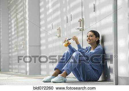 Stock Image - Hispanic nurse eating fruit on floor. Fotosearch