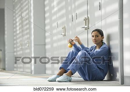 Stock Photo - Hispanic nurse eating fruit on floor. Fotosearch