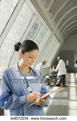 Picture - Hispanic nurse reviewing medical chart in corridor. Fotosearch