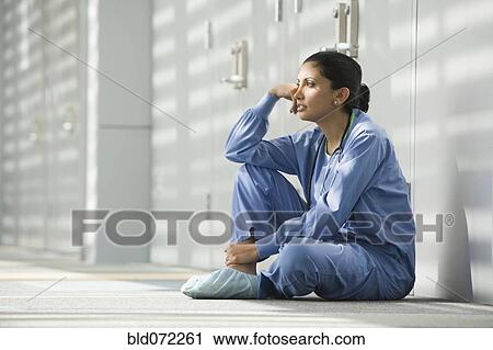 Stock Image - Hispanic nurse sitting on floor with head in hands. Fotosearch