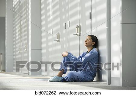 Stock Image - Hispanic nurse with eyes closed sitting on floor. Fotosearch