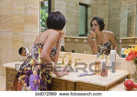 Stock Photo - Hispanic woman applying lipstick in bathroom mirror. Fotosearch
