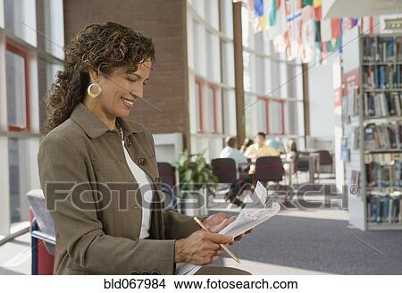 Picture - Hispanic woman reading paperwork in library. Fotosearch