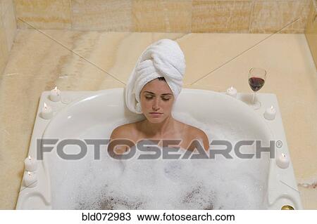 Stock Image - Hispanic woman relaxing in bubble bath. Fotosearch