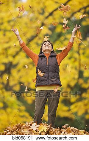 Stock Image - Hispanic woman throwing autumn leaves. Fotosearch
