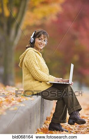 Hispanic woman using laptop outdoors with headphones View Large Photo Image Picture - Hispanic woman using laptop outdoors with headphones. Fotosearch