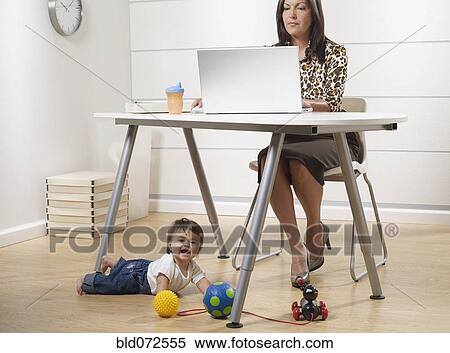 Stock Photography - Hispanic working mother and baby son in home office. Fotosearch