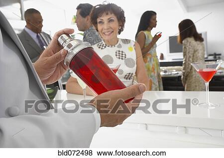 Stock Photo - Host mixing martini cocktails at party. Fotosearch