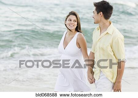 Stock Photo - Husband holding hands with pregnant wife on beach. Fotosearch