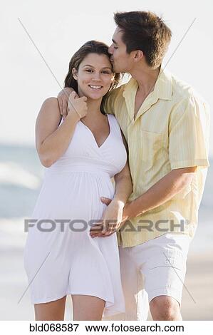 Stock Photo - Husband hugging pregnant wife on beach. Fotosearch