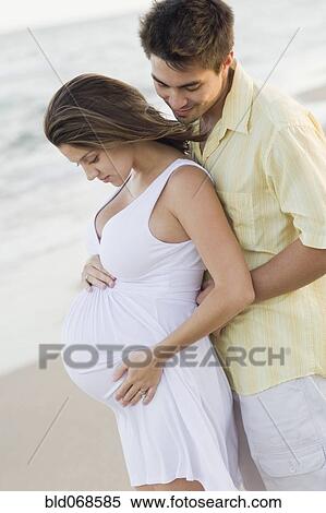 Stock Photography - Husband hugging pregnant wife on beach. Fotosearch