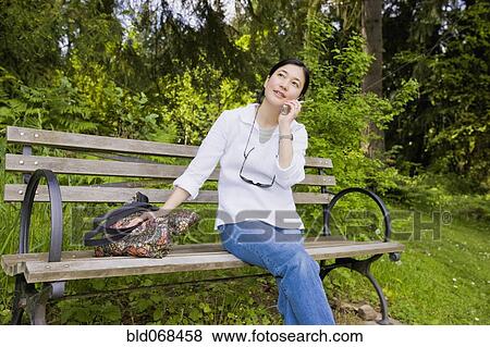Stock Photo - Japanese woman using cell phone in park. Fotosearch