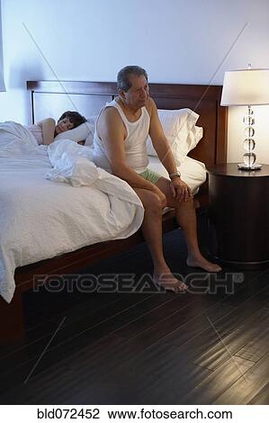 Stock Image - Man in bedroom waking up in the morning. Fotosearch