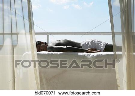 Stock Image - Man laying on massage table on balcony. Fotosearch