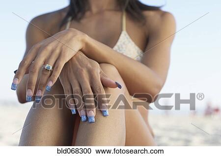 Stock Image - Midsection of mixed race woman sitting on beach. Fotosearch