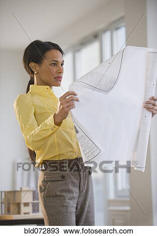 Stock Image - Mixed race architect examining blueprint. Fotosearch