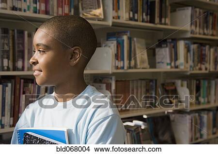 Picture - Mixed race boy holding books in library. Fotosearch