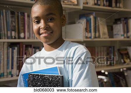 Stock Image - Mixed race boy holding books in library. Fotosearch