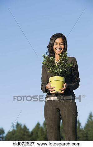 Mixed race businesswoman holding potted plant View Large Photo Image Stock Photo - Mixed race businesswoman holding potted plant. Fotosearch