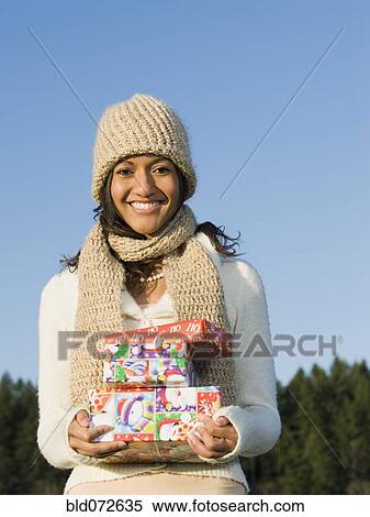 Stock Photography - Mixed race businesswoman holding Christmas gifts. Fotosearch