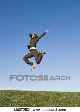 Mixed race businesswoman jumping in field View Large Photo Image Picture - Mixed race businesswoman jumping in field. Fotosearch