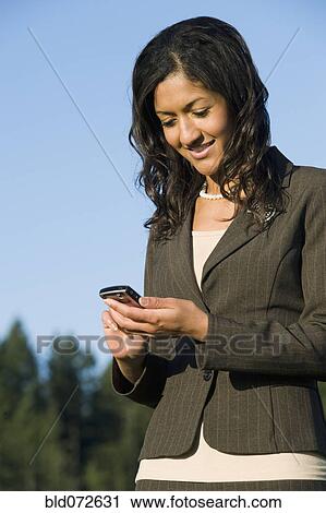 Stock Image - Mixed race businesswoman text messaging with cell phone. Fotosearch