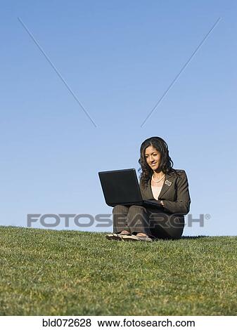 Mixed race businesswoman using laptop in grass View Large Photo Image Stock Photo - Mixed race businesswoman using laptop in grass. Fotosearch