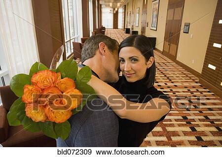 Stock Photo - Mixed race couple hugging and holding bouquet of flowers. Fotosearch