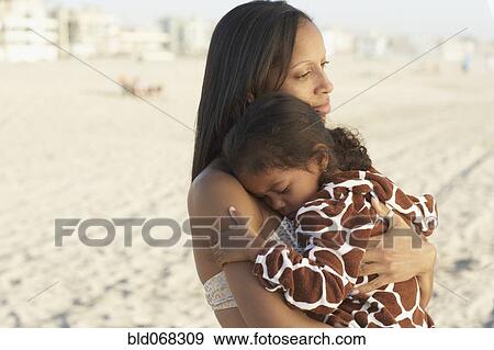 Stock Photo - Mixed race mother holding daughter at beach. Fotosearch