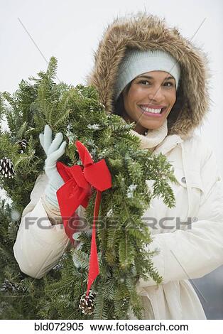 Stock Photography - Mixed race woman carrying Christmas wreath. Fotosearch