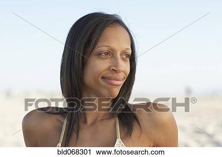 Stock Image - Mixed race woman relaxing at beach. Fotosearch