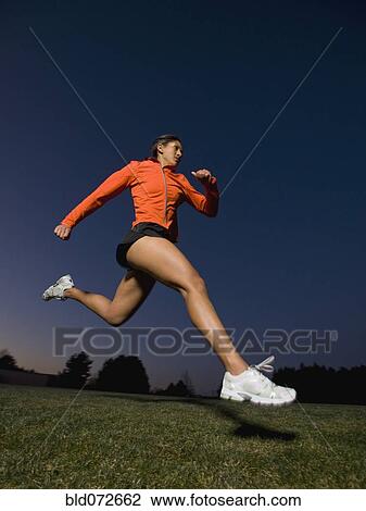 Stock Image - Mixed race woman running on grass. Fotosearch