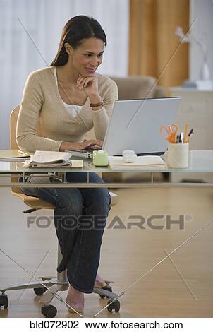 Stock Image - Mixed race woman using laptop in home office. Fotosearch