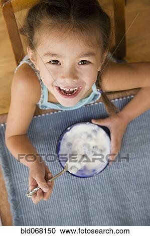 Stock Image - Mixed race young girl eating yogurt with spoon. Fotosearch