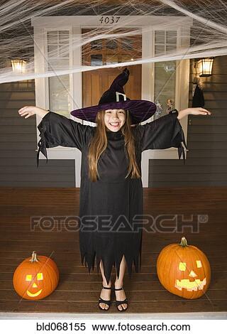 Stock Photography - Mixed race young girl in witch costume with Halloween pumpkins. Fotosearch