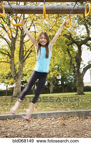 Stock Photo - Mixed race young girl swinging from playground equipment. Fotosearch