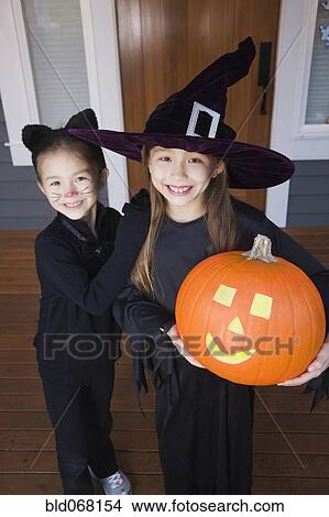 Picture - Mixed race young girls in cat and witch costumes. Fotosearch