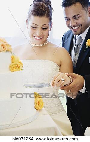Picture - Multi-ethnic bride and groom cutting cake. Fotosearch
