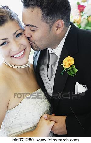 Stock Image - Multi-ethnic bride and groom kissing. Fotosearch